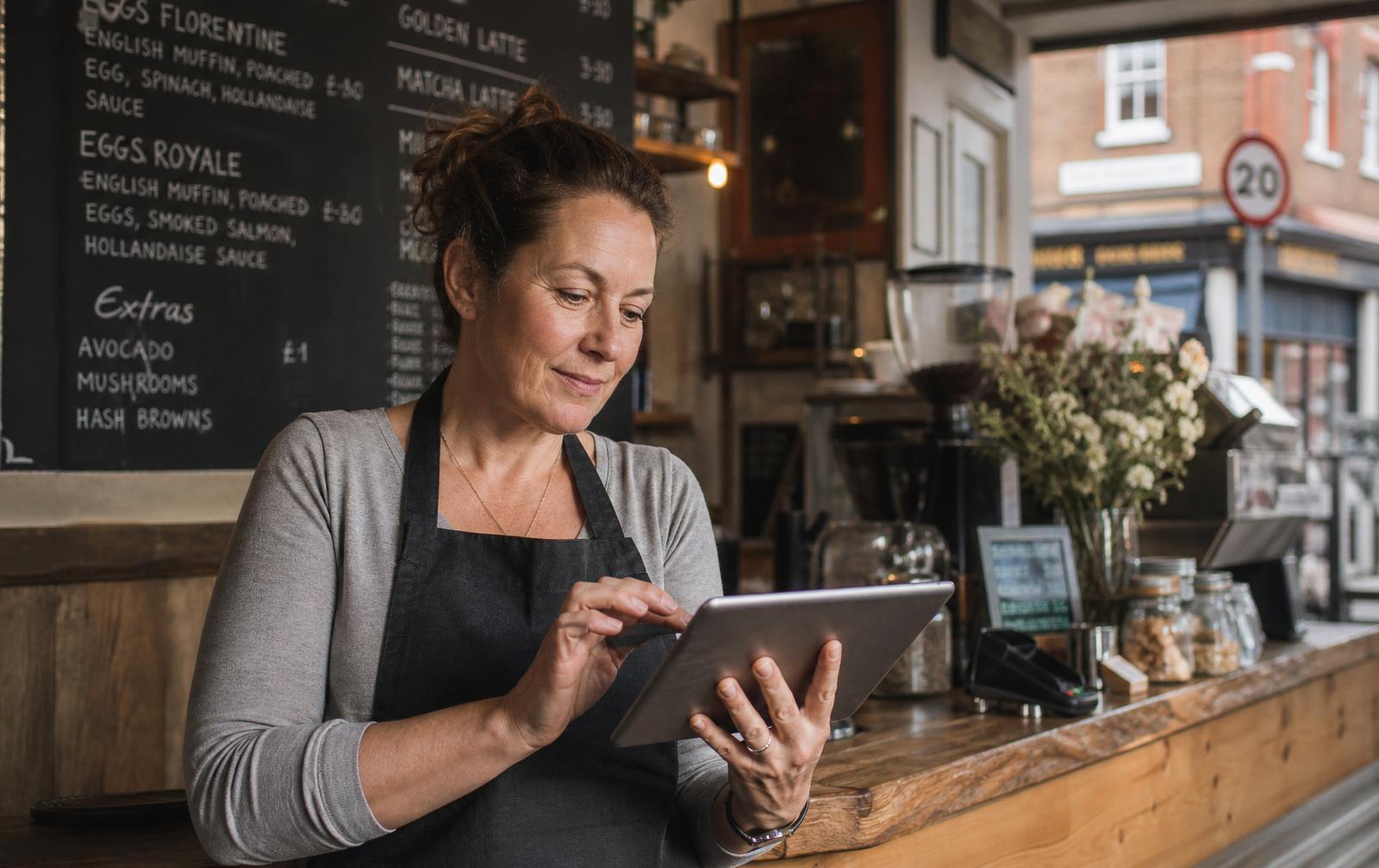 Independent London cafe owner reviewing business finance options on a tablet at her counter